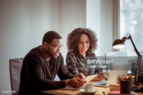 two designers using a digital tablet together and smiling - afro friends home stock pictures, royalty-free photos & images