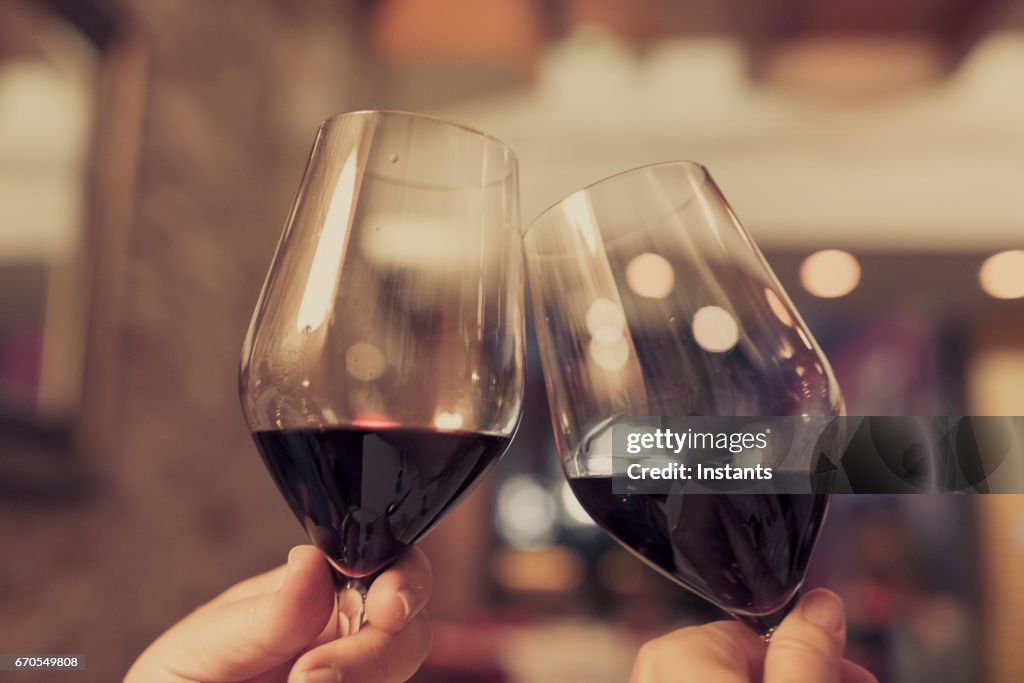 Casal celebrando e torcendo em boas notícias, com cada um copo de vinho tinto em suas mãos.