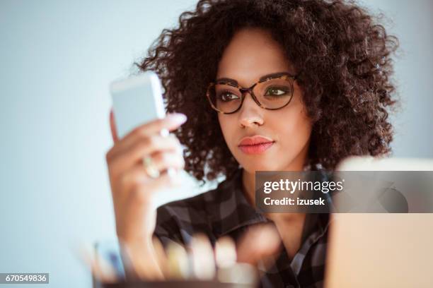 young african woman with glasses using mobile phone - concentration curl stock pictures, royalty-free photos & images