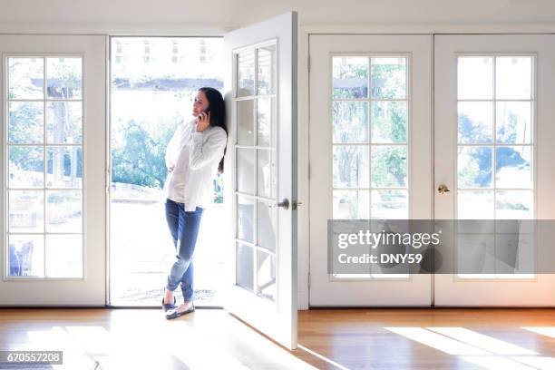 hispanic female millennial using mobile phone while working at home - french doors stock pictures, royalty-free photos & images