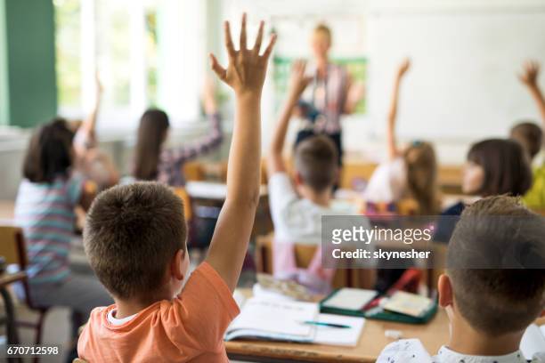 rückansicht des schuljunge hand heben, die frage zu beantworten. - primary school teacher stock-fotos und bilder