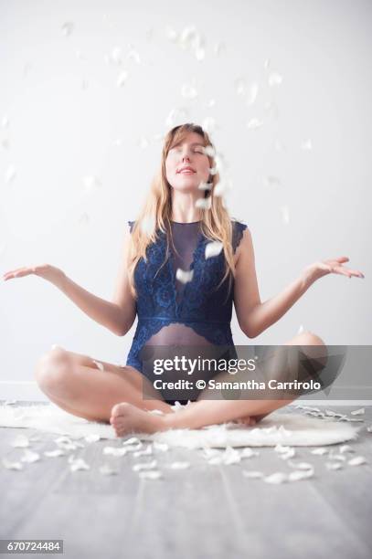 donna incinta seduta su un tappeto bianco. intimo / body blu. petali bianchi per terra e in aria. - capelli lisci fotografías e imágenes de stock