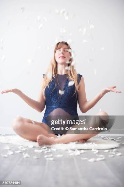 donna incinta seduta su un tappeto bianco. intimo / body blu. petali bianchi per terra e in aria. - crescita stock pictures, royalty-free photos & images