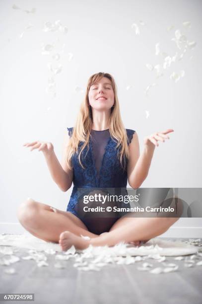 donna incinta seduta su un tappeto bianco. intimo / body blu. petali bianchi per terra e in aria. - capelli lisci fotografías e imágenes de stock