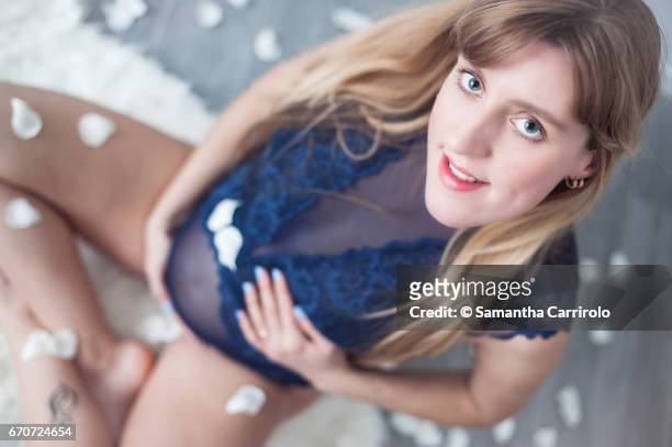 donna incinta seduta su un tappeto bianco. mani sul pancione. intimo / body blu. petali bianchi per terra e in aria. - caucasico stock-fotos und bilder