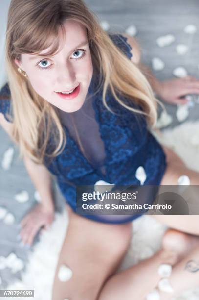 donna incinta seduta su un tappeto bianco. intimo / body blu. petali bianchi per terra e in aria. - capelli lisci fotografías e imágenes de stock