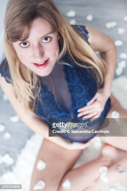 donna incinta seduta su un tappeto bianco. mani sul pancione. intimo / body blu. petali bianchi per terra e in aria. - sorridere stock-fotos und bilder