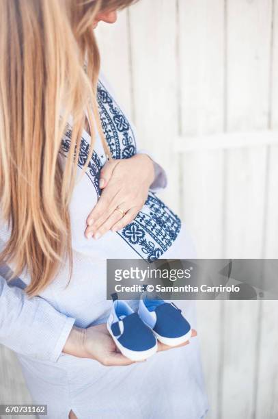 donna incinta. mano sul pancione. camicia a righe con ricamo. scarpine blu in mano. - crescita stock pictures, royalty-free photos & images