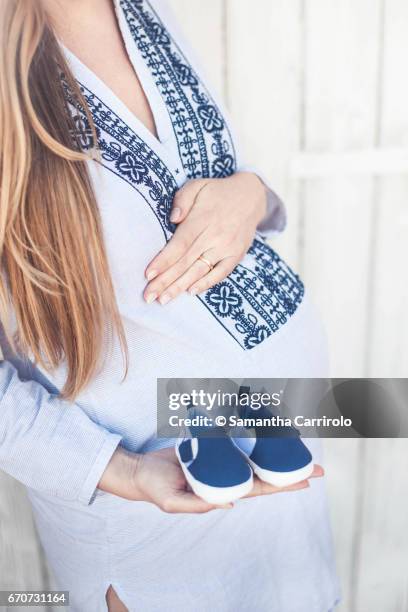 donna incinta. mano sul pancione. camicia a righe con ricamo. scarpine blu in mano. - capelli lisci fotografías e imágenes de stock