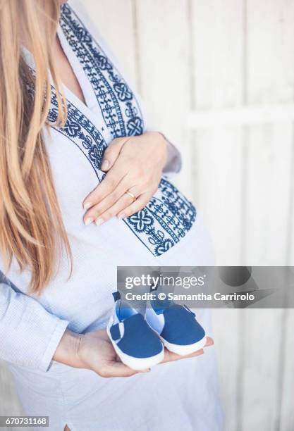 donna incinta. mano sul pancione. camicia a righe con ricamo. scarpine blu in mano. - aspettare fotografías e imágenes de stock