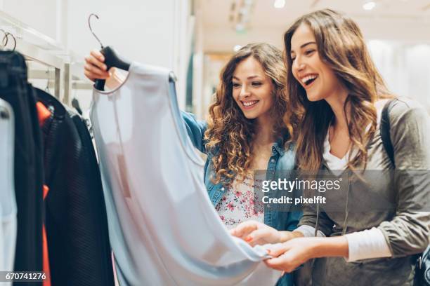 two cheerful girls shopping for clothes - buying stock pictures, royalty-free photos & images