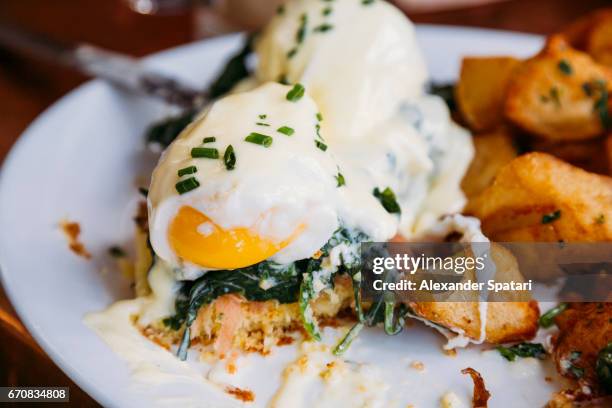 close up of eggs benedict with liquid egg yolk and bechamel sauce, served with potato - eggs benedict stock pictures, royalty-free photos & images