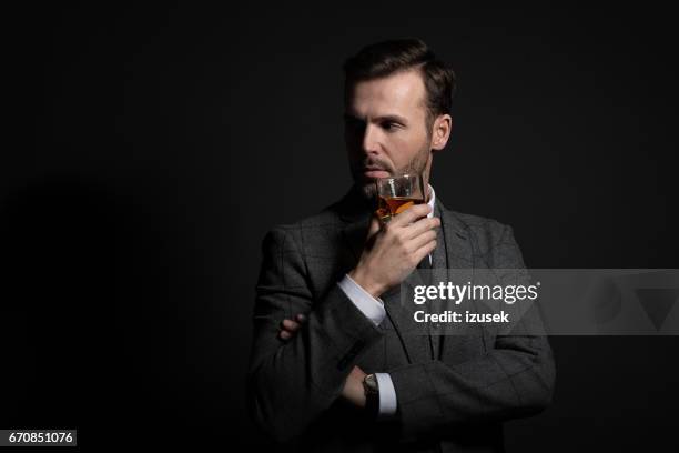 portrait of elegant man drinking whiskey - drinking whiskey stock pictures, royalty-free photos & images