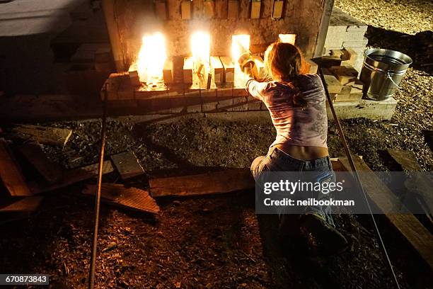 woman tending to fire of wood kiln at night - 火をたく ストックフォトと画像