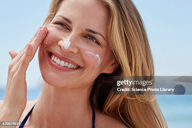 woman applying sun cream to face - sun on face stock-fotos und bilder