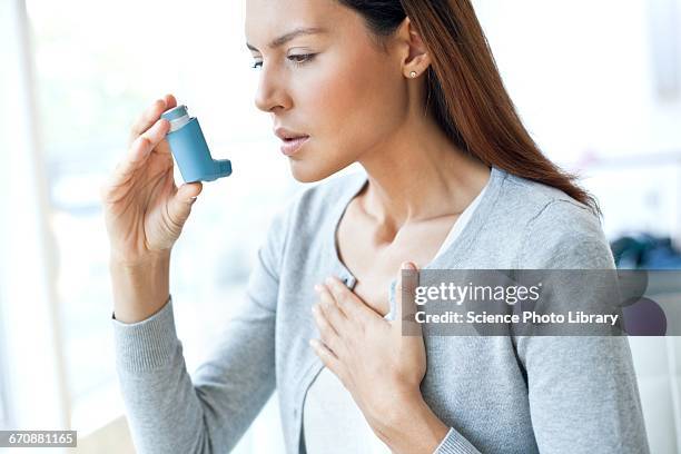 young woman using inhaler touching chest - asthma stockfoto's en -beelden