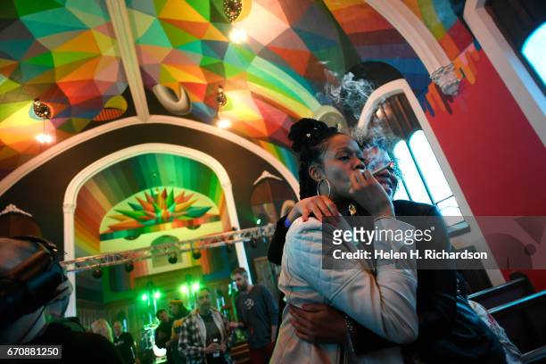 Andrea Camp, left, of Chicago, hugs Kimm Miller, right, from Lakewood, as she smokes from a pipe as the two participate in 4/20 celebration services...