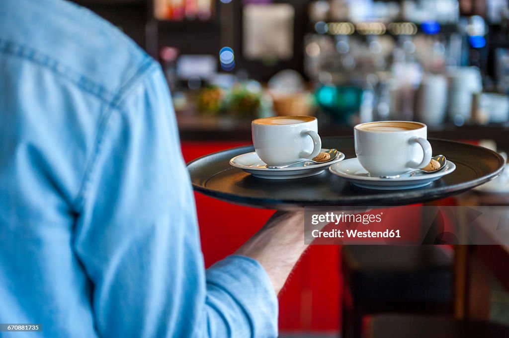 Waiter carrying tray with cappuccino cups in a cafe