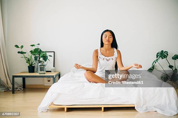 young woman practicing yoga on bed - meditation sitting foto e immagini stock