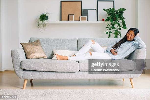 young woman relaxing on couch in the living room using smartphone - women sitting stock pictures, royalty-free photos & images