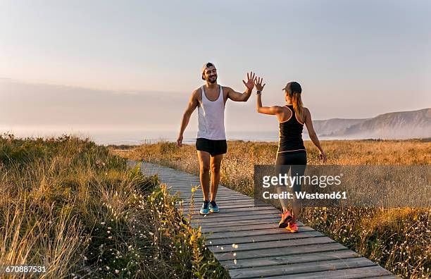 spain, aviles, athletes couple hitting five on the beach in the evening - two woman running fotografías e imágenes de stock
