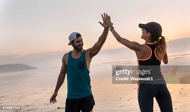 athletes couple hitting five on the beach at sunset - choque de manos en el aire fotografías e imágenes de stock