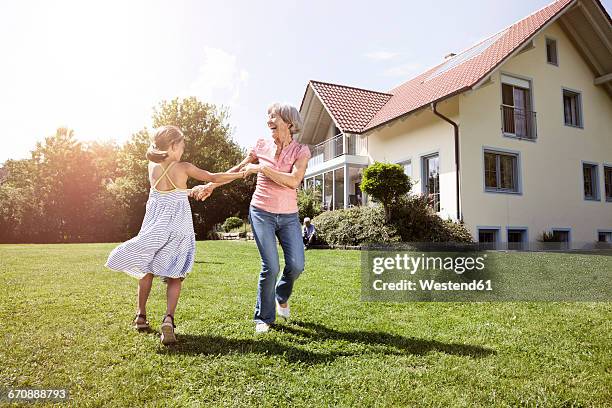 playful grandmother with granddaughter in garden - enkelkind stock-fotos und bilder