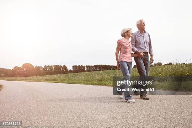 smiling senior couple walking on country road - gemeinsam gehen stock-fotos und bilder