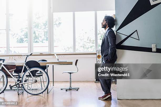 young creative businessman standing in office, thinking with hands in pockets - fundador fotografías e imágenes de stock