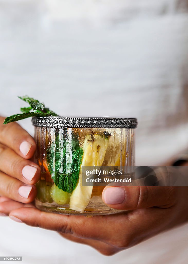 Woman's hands holding glass of Sangria with pineapple and mint