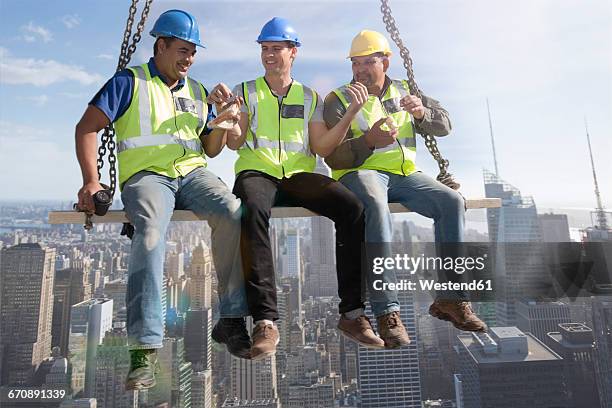 three construction workers sitting on suspended scaffolding high above city having lunch - scaffolding fotografías e imágenes de stock