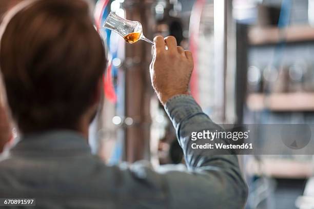 man in distillery examining glass with liquor - destillation stock-fotos und bilder