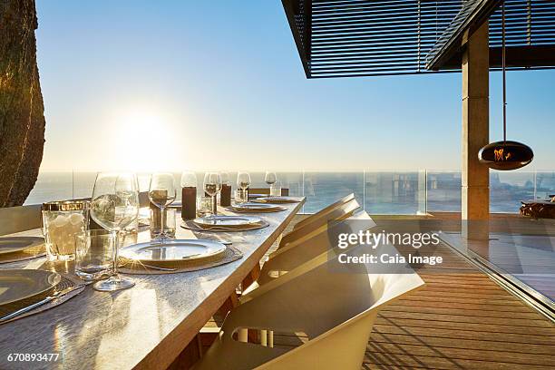 sun shining over ocean behind luxury patio dining table with placesettings - beach house balcony stock pictures, royalty-free photos & images