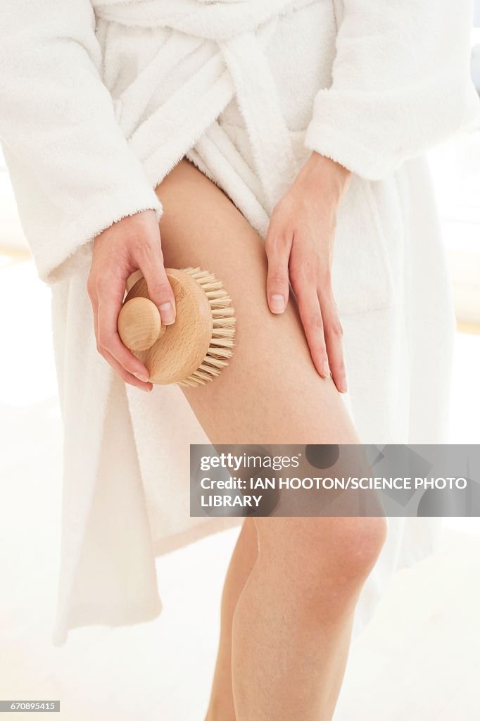 Young woman using body brush on leg