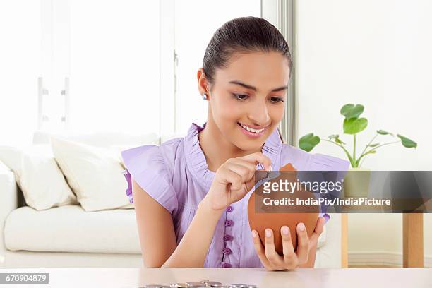 smiling teenage girls holding a money bank in her hand and dropping a coin in the slot - gullak bildbanksfoton och bilder