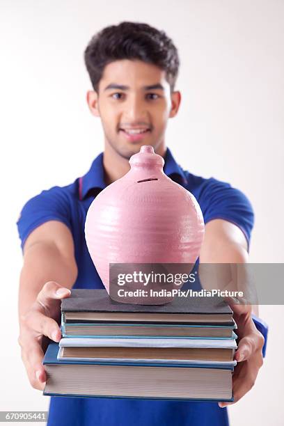 young college student holding stack of books with a money bank - gullak stock-fotos und bilder