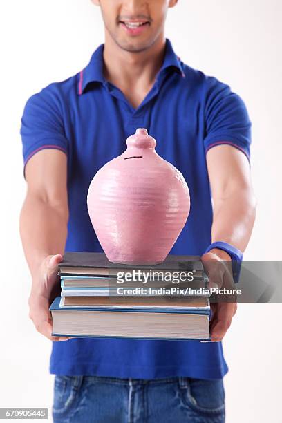 young college student holding stack of books with a money bank - gullak stock-fotos und bilder