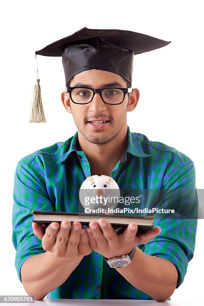 young college student holding stack of books with a small piggy bank - gullak bildbanksfoton och bilder