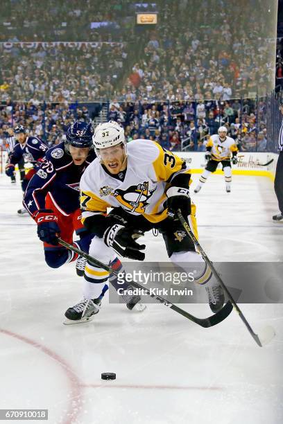 Carter Rowney of the Pittsburgh Penguins and Gabriel Carlsson of the Columbus Blue Jackets skate after the puck in Game Four of the Eastern...