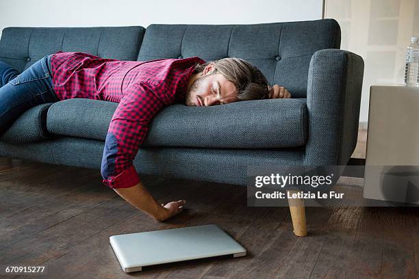 young man sleeping on sofa with laptop - allongé sur le devant photos et images de collection