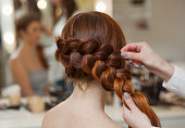 red-haired hairy girl, hairdresser weaves a French braid