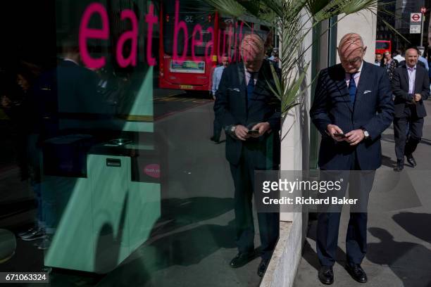 Businessman checks his messages beneath the shadows of a potted plant outside an Itsu shop in the Square Mile, the capital's financial district, on...