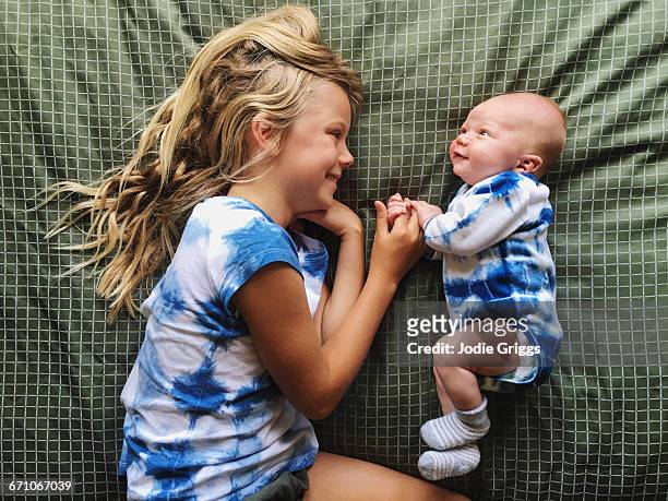 smiling infant lying down with older sibling - sisters stock-fotos und bilder