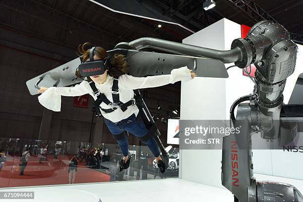 This photo taken on April 19, 2017 shows a woman trying out a virtual wing flight experience on the Nissan stand at the Shanghai International...