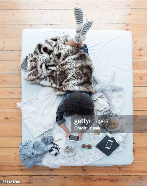 woman lying on bed using tablet pc - lying on a bed stock pictures, royalty-free photos & images
