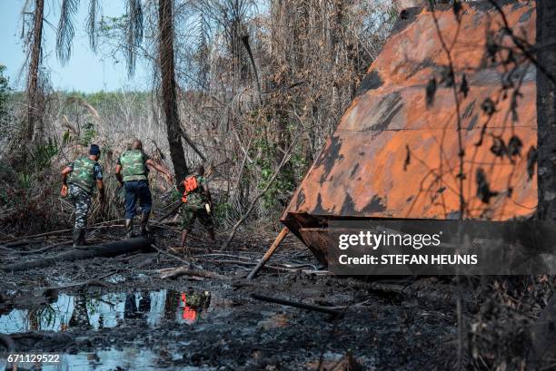 Members of the NNS Delta of the Nigerian Navy forces walk through the oil soaked land at a destroyed illegal oil refinery on April 19, 2017 in the...