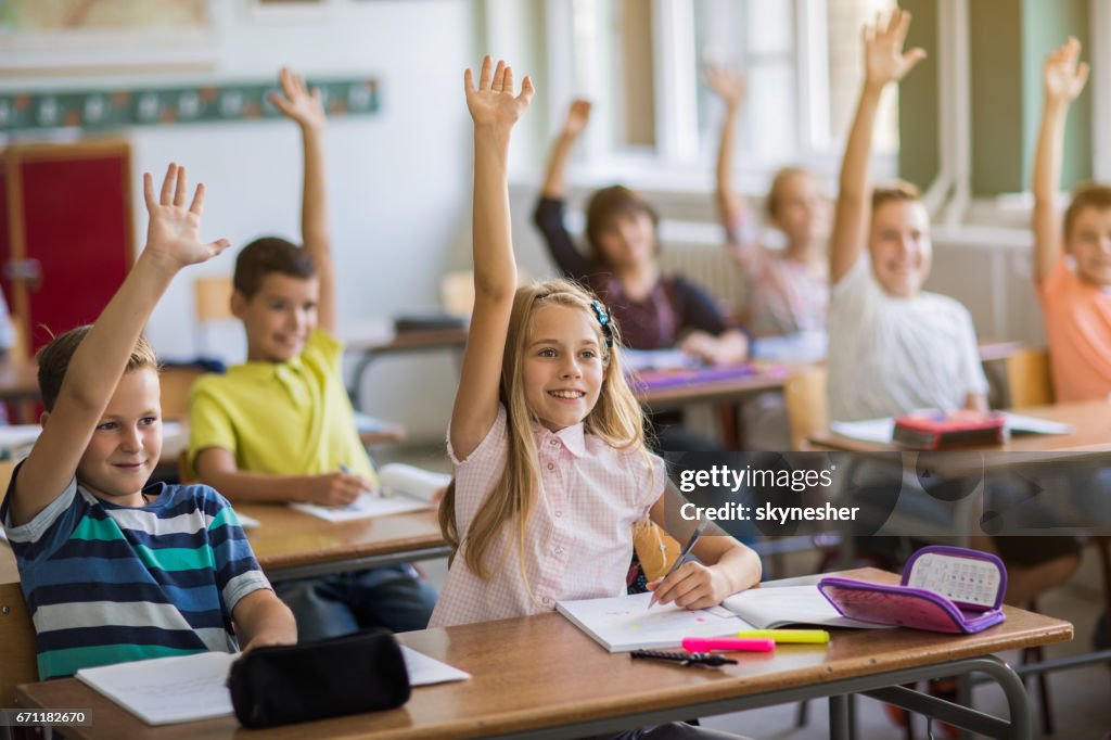 Gruppe der glückliche Schulkinder mit erhobenen Armen im Klassenzimmer.