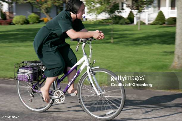 An Amish teen girl riding a bicycle barefoot.