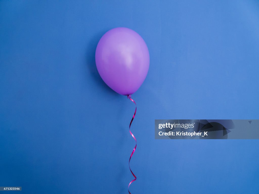 Single pink balloon on blue background.