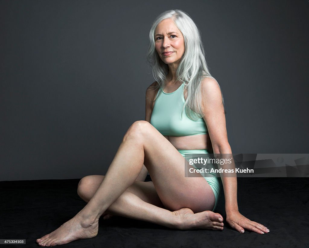 Grey haired woman in swimsuit, sitting down.
